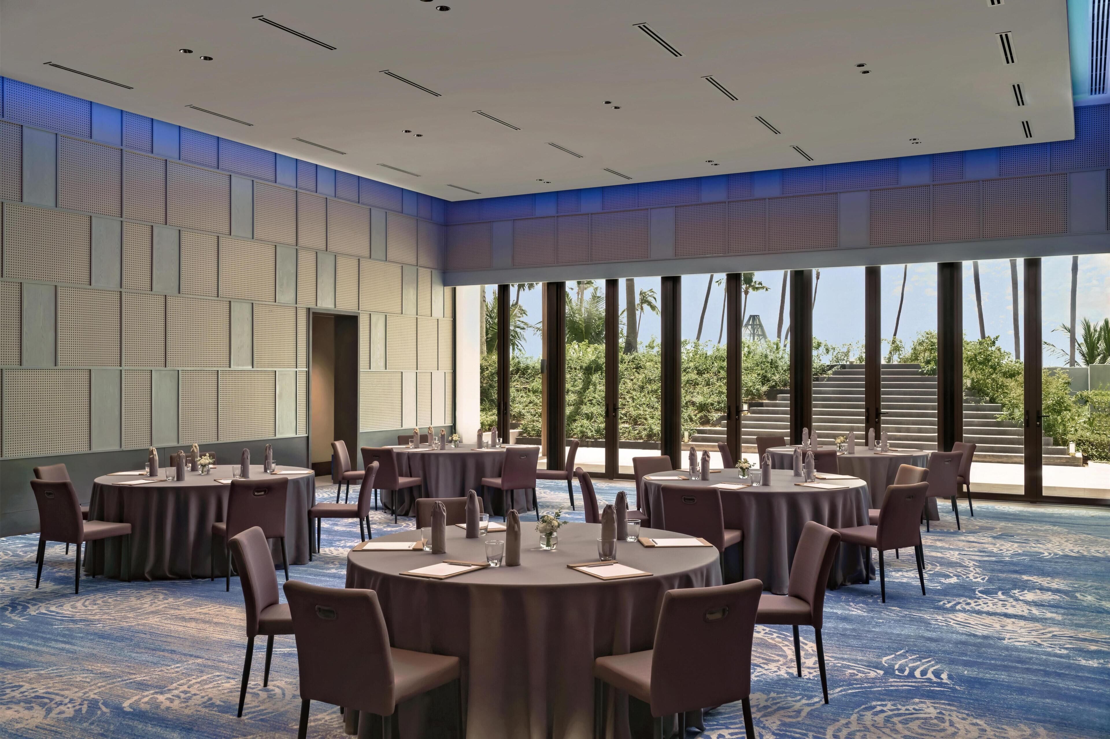 Un salón de conferencias con mesas redondas, sillas y alfombra azul.