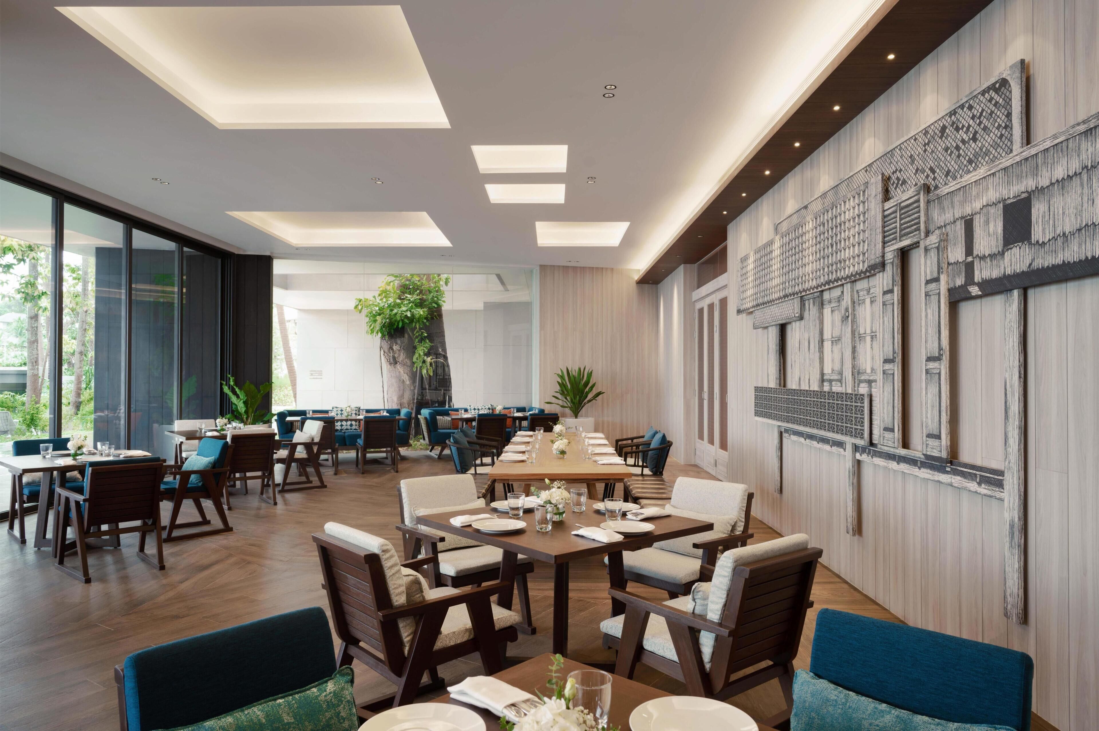 A modern dining area with a long table, multiple chairs, and a large window.