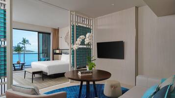 A hotel room with a bed, a sofa, a TV, a table with books, and a view of the sea.
