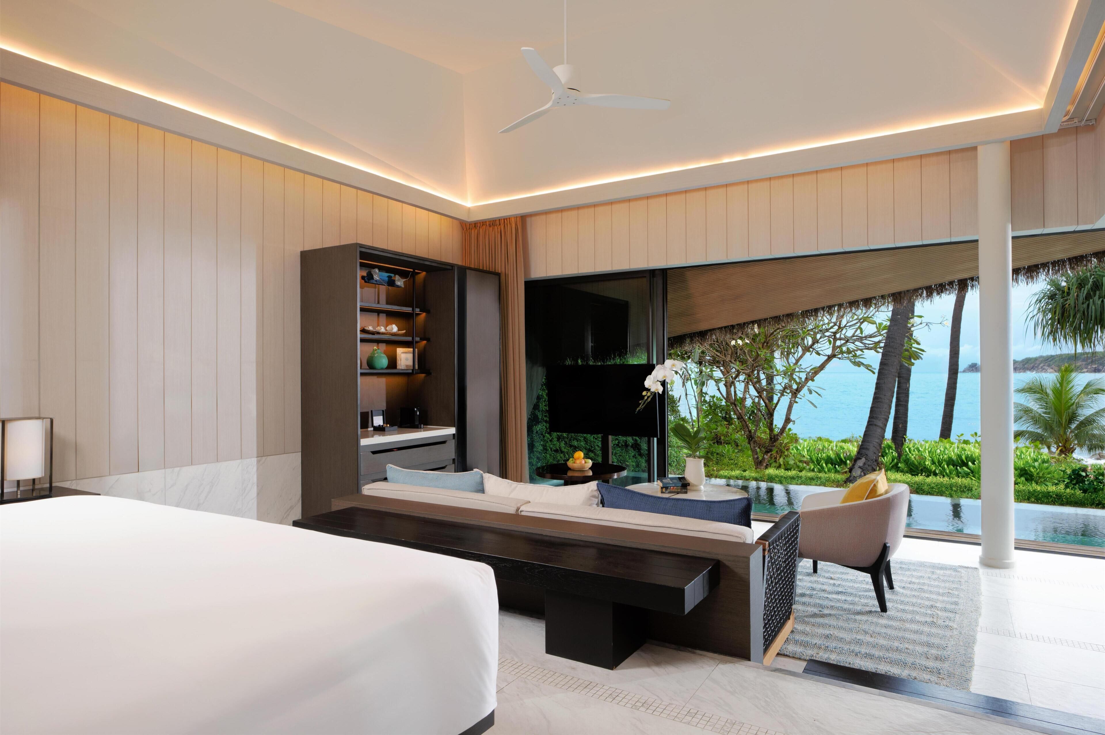 Habitación de hotel moderna con cama, zona de estar, televisor y ventana grande con vista al océano.