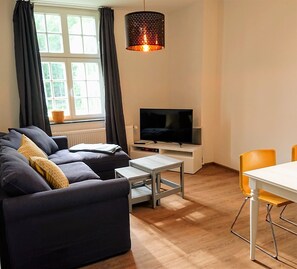 Ein modernes Wohnzimmer mit einer Couch, einem Fernseher, einem Tisch und einer Essecke mit Stühlen.