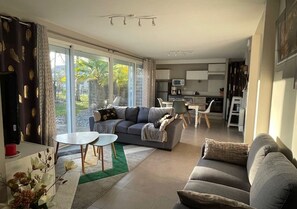 Ein modernes Wohnzimmer mit einem grauen Sofa, einem Couchtisch und einem Essbereich mit kleinem Tisch und Stühlen.