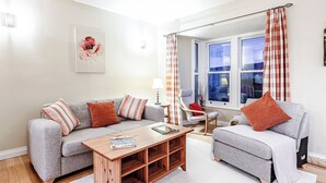 A modern living room with a grey sofa, a wooden coffee table, and a window with curtains.