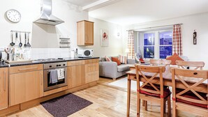 A modern kitchen with wooden cabinets, a built-in oven, and a microwave. There is a dining area with a wooden table and chairs.