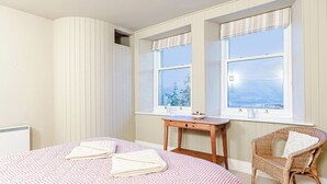 A bedroom with a bed, two windows, a chair, and a small table.