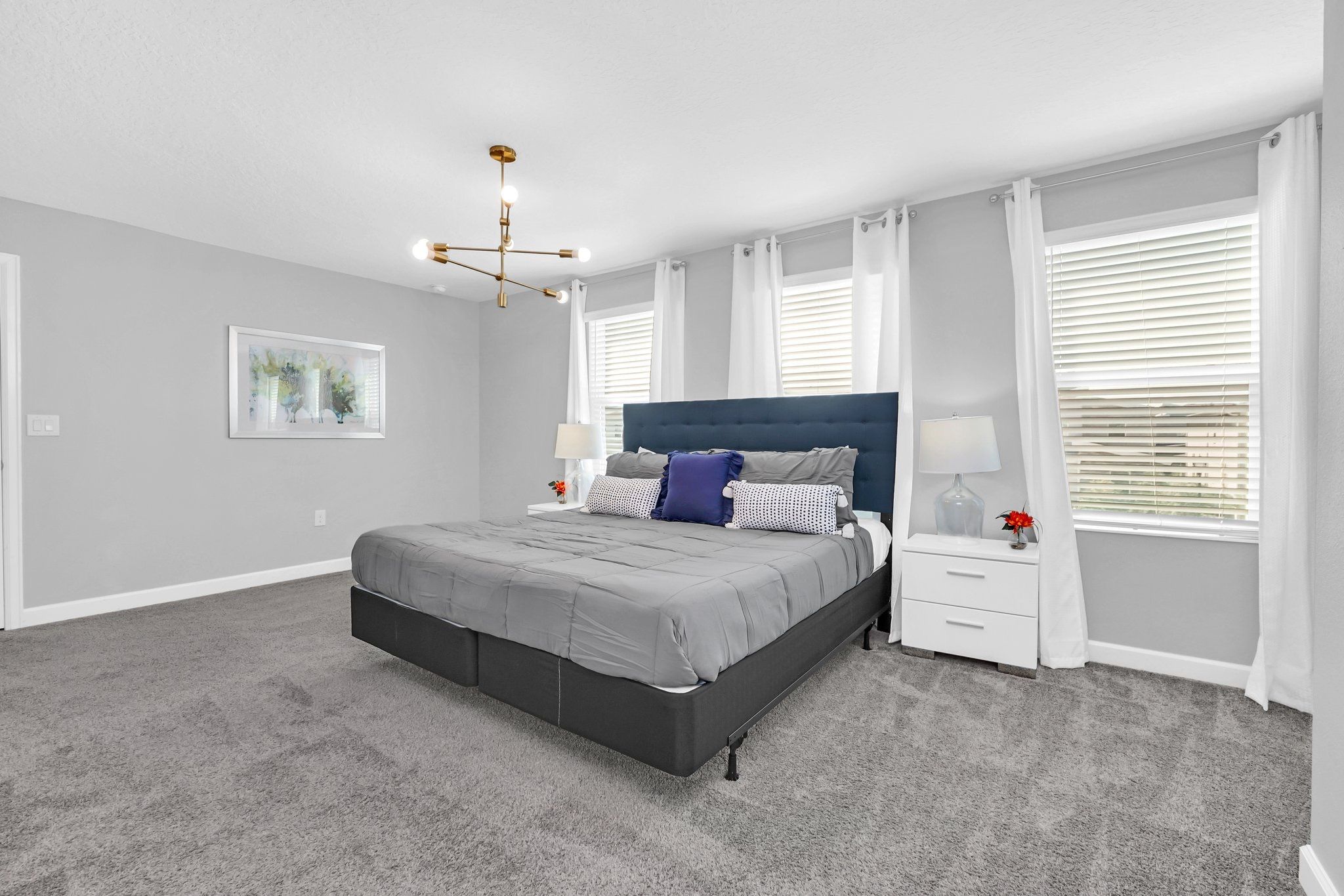 Une chambre à coucher avec un lit, des tables de chevet, un lustre et une fenêtre avec des stores.