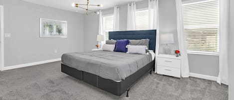 A bedroom with a bed, nightstands, a chandelier, and a window with blinds.