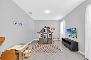 A modern living room with a playhouse, a dining area, a television, and a chevron-patterned rug.
