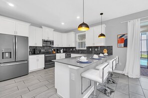 A modern kitchen with stainless steel appliances, a central island with bar stools, and pendant lighting.