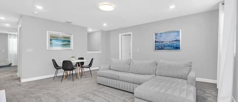 En moderne stue med en grå sofa, et spisebord med stole og to billeder hængende på væggene.