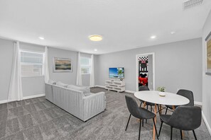 A modern living room with a grey sofa, a dining table with chairs, and a TV on the wall.