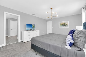 A bedroom with a bed, a dresser, a television, and a ceiling light fixture.