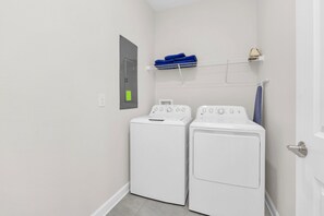 A laundry room with two white washing machines and a shelf above them holding folded clothes.