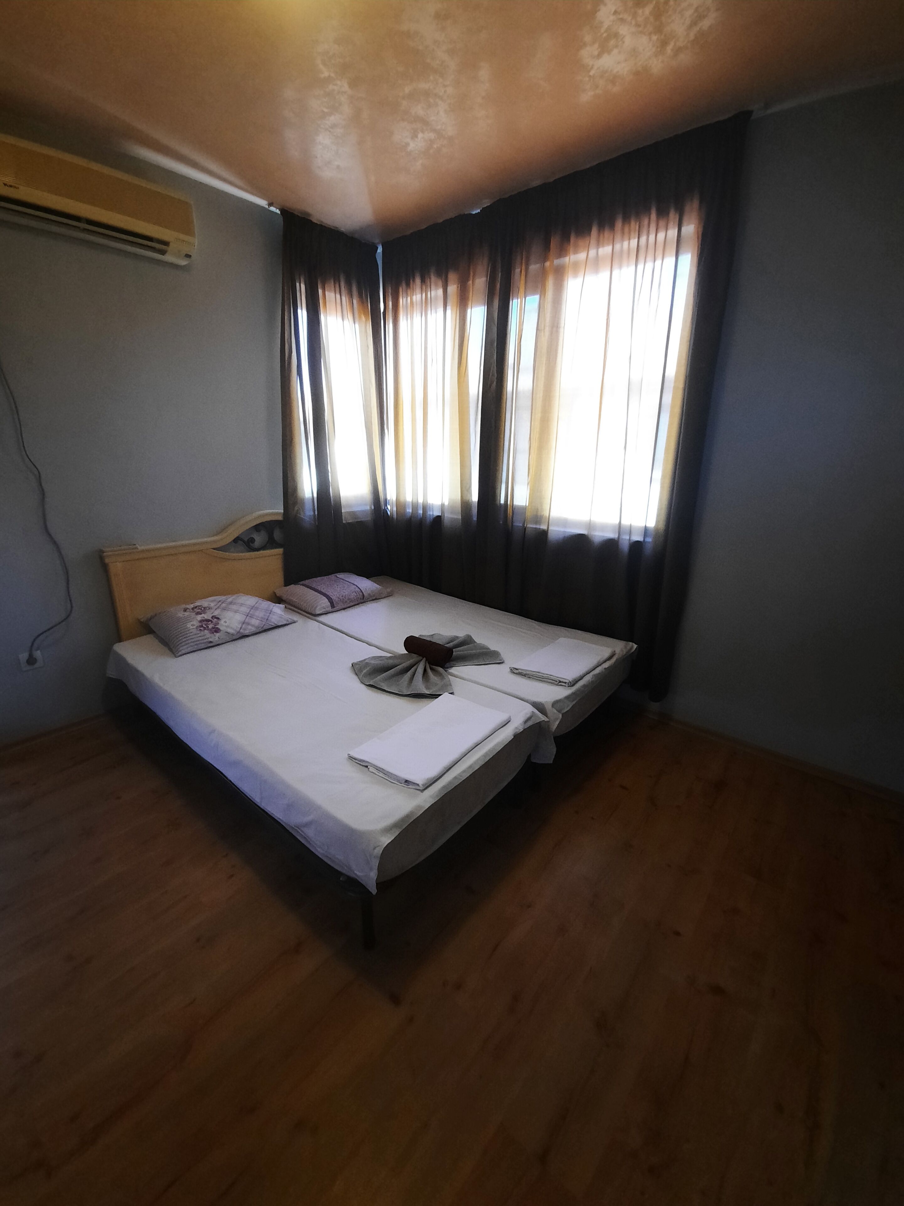 Une chambre comprenant un lit, une tête de lit, une fenêtre avec des rideaux et un appareil de climatisation.