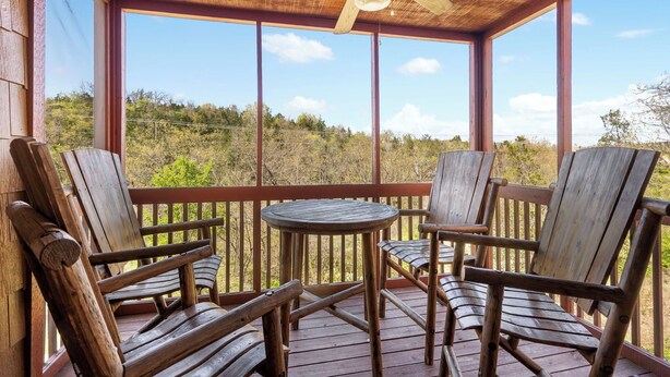 A wooden deck with four Adirondack chairs and a round table, overlooking a natural landscape. - Woodland Retreat for 6 | Cozy Fireplace + Pool Access (Branson)