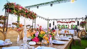 Un espace de restauration en plein air, avec des tables en bois dressées pour un repas, entourées de chaises et agrémentées de compositions florales.
