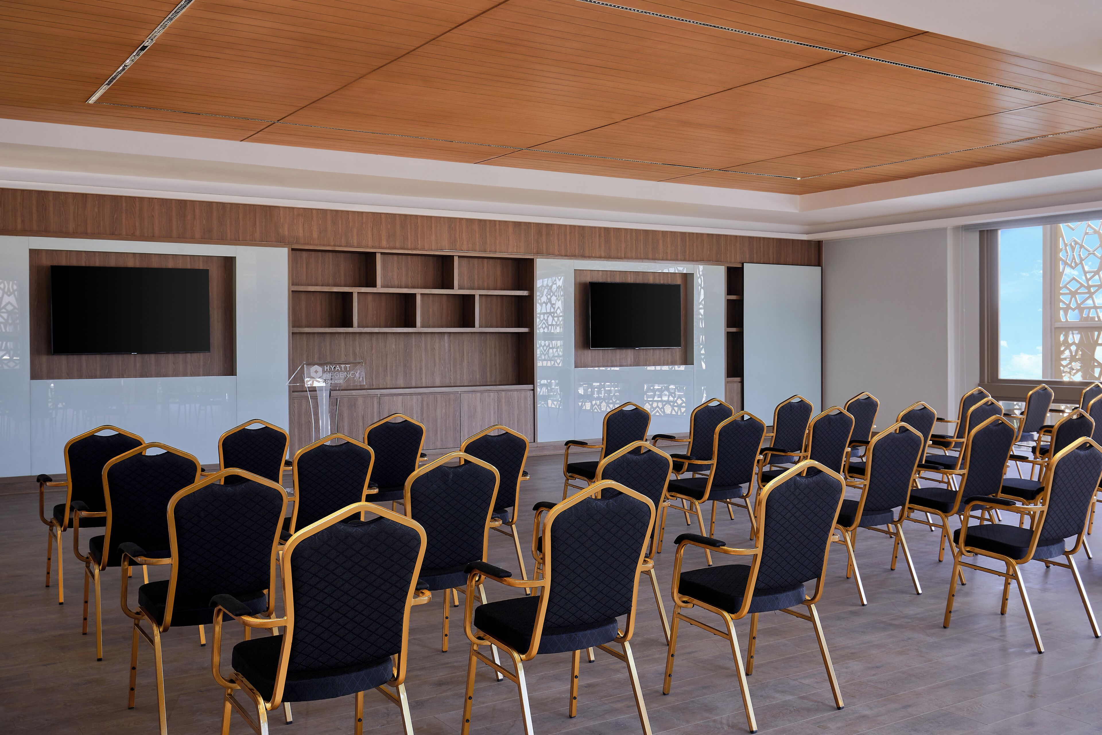 Un salón de conferencias con filas de sillas, una pantalla grande y un revestimiento de madera en la pared.