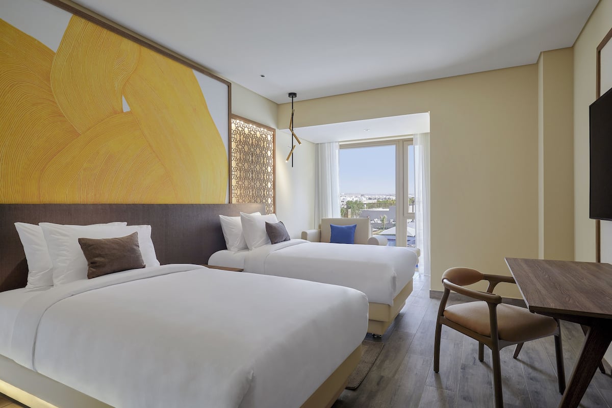 A hotel room with two beds, a desk, and a view of the city.