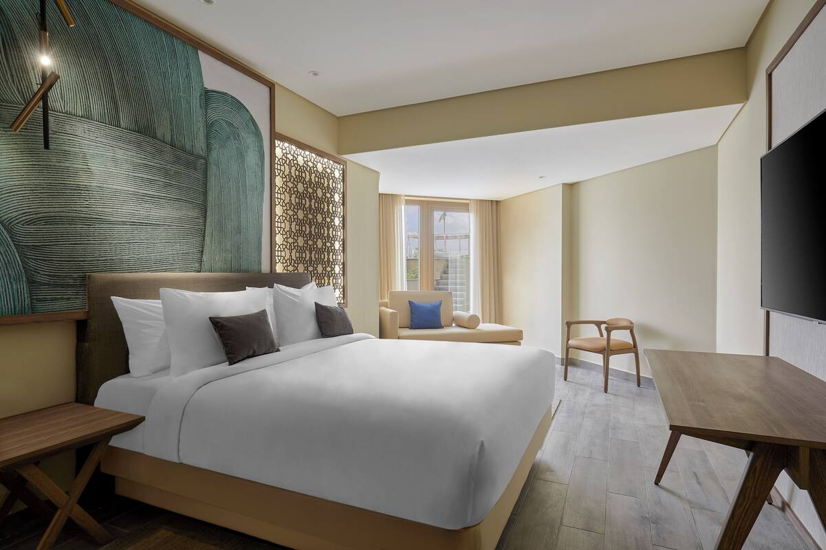 A modern hotel room with a large bed, a wooden desk, a chair, and a TV.