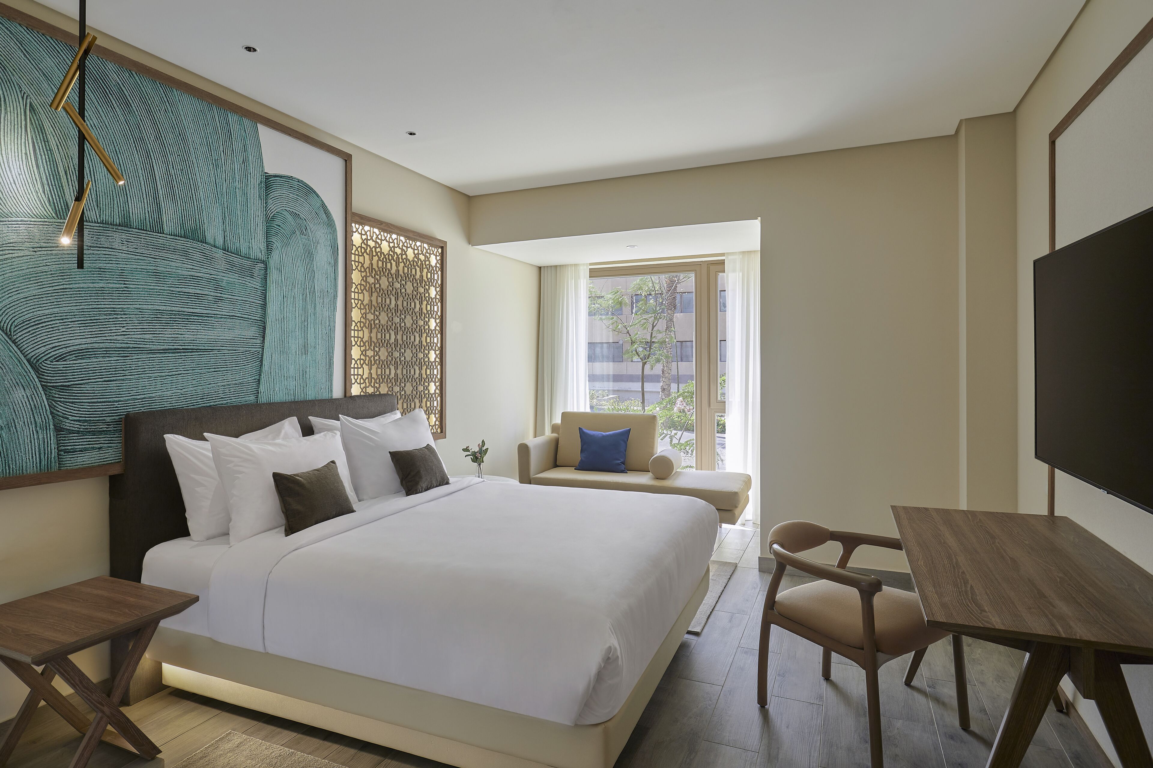 A modern hotel room with a large bed, a desk, a chair, and a TV.