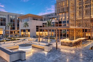 An outdoor seating area with a bar, palm trees, and a modern building with large windows. - Hyatt Regency Cairo West (6th of October City)