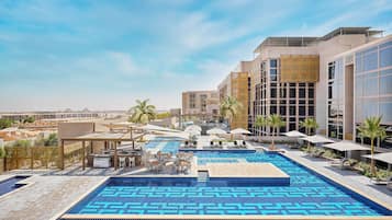 A rooftop pool area with a geometric tile pattern, lounge chairs, umbrellas, and a view of the surrounding buildings.
