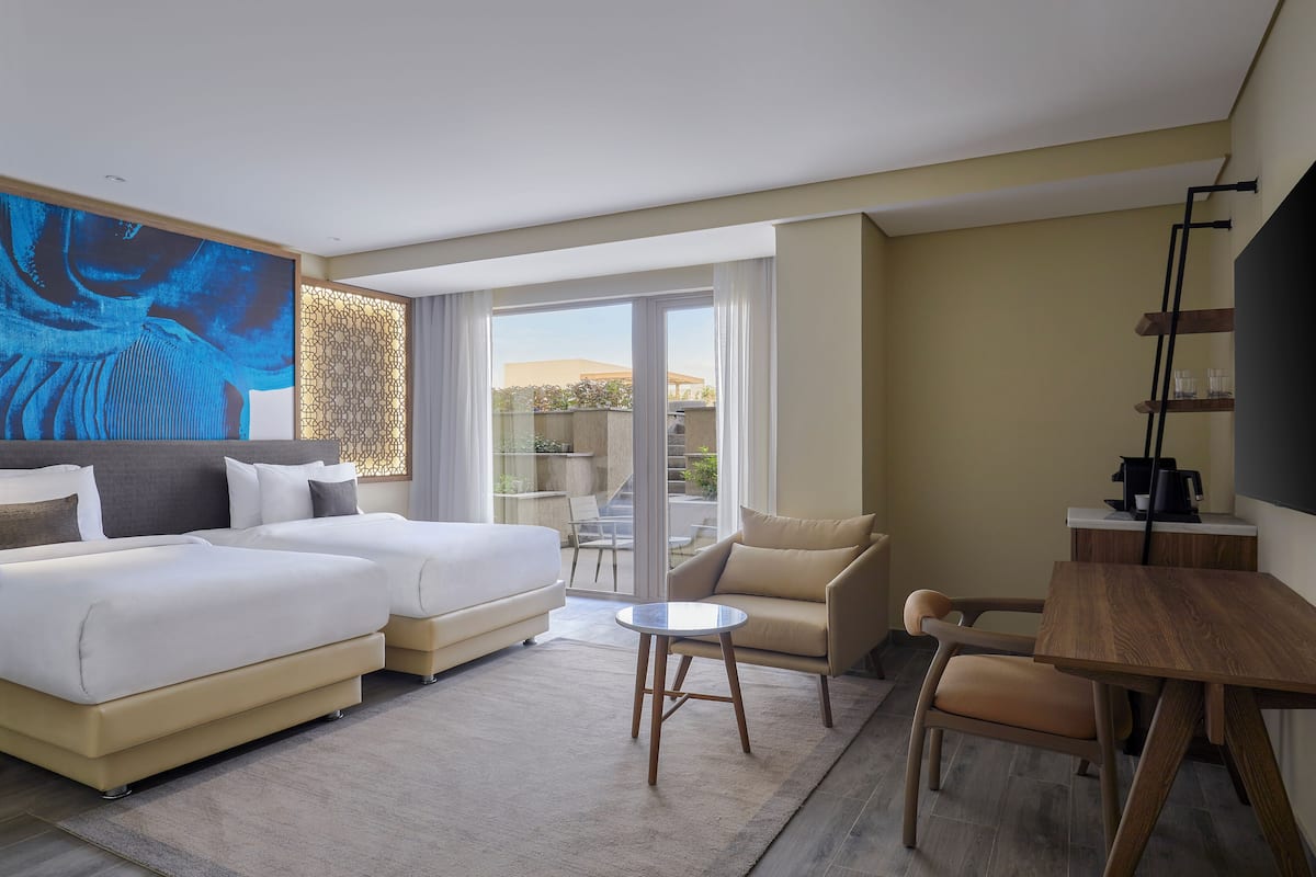 A modern hotel room with a large bed, a sofa, a small table, and a balcony with a view.