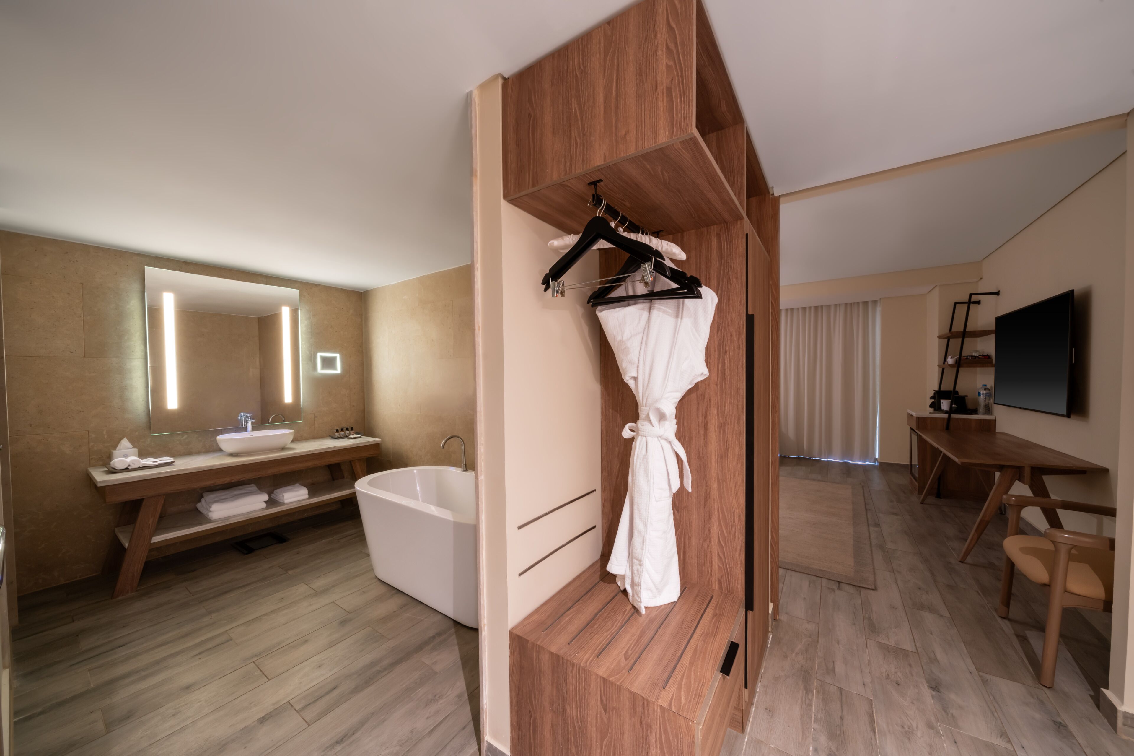 A modern bathroom with a large mirror, wooden vanity, bathtub, and a robe hanging on a rack.