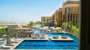 A rooftop pool area with multiple pools, lounge chairs, umbrellas, and a view of the cityscape. - Hyatt Regency Cairo West (6th of October City)