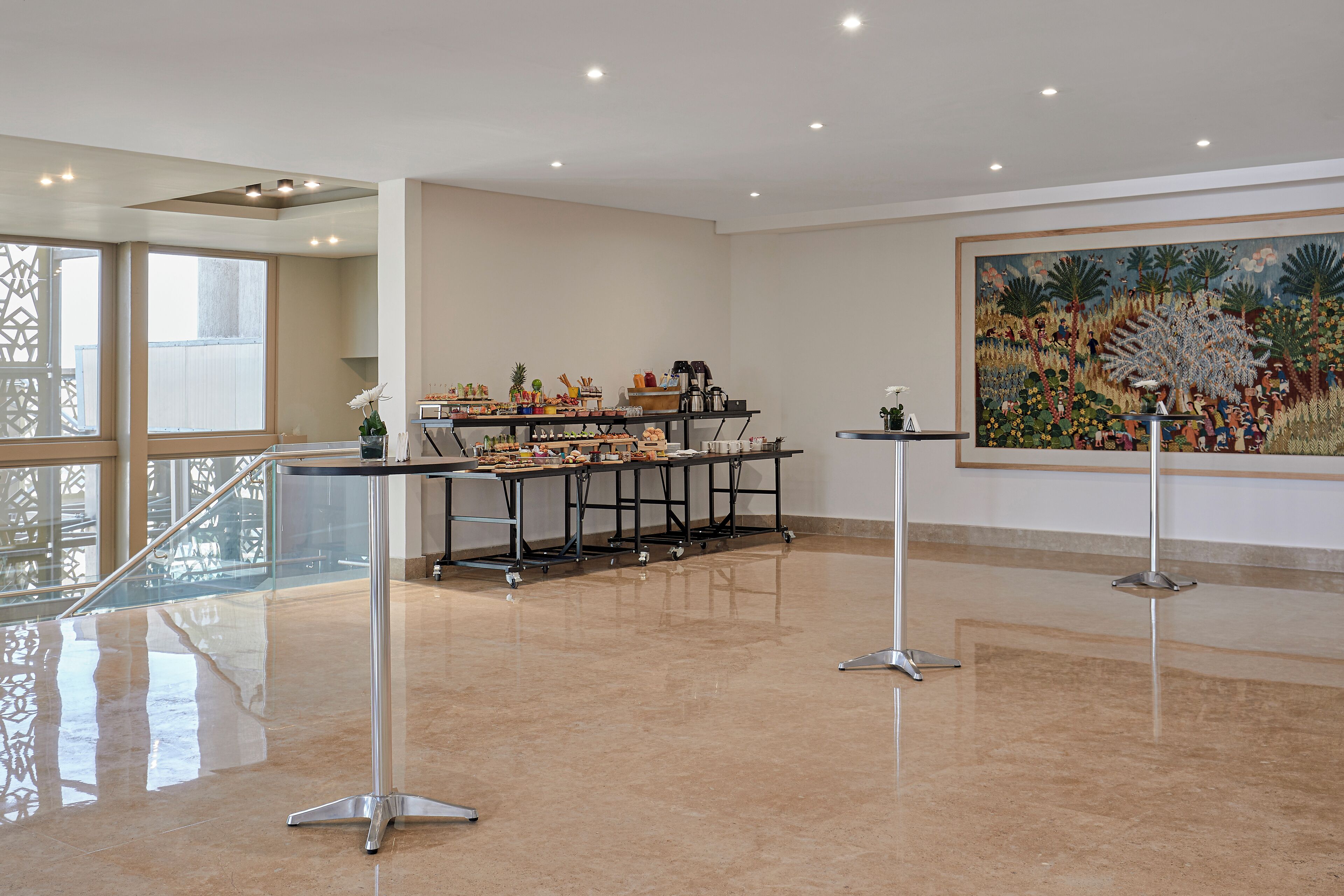 Eine geräumige Lobby mit hochglänzendem Boden, einem Empfangstresen, einer Kaffeestation und einem großen Wandgemälde.
