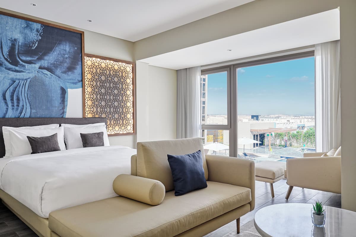 A modern hotel room with a large bed, a sofa, a small table, and a view of the city.