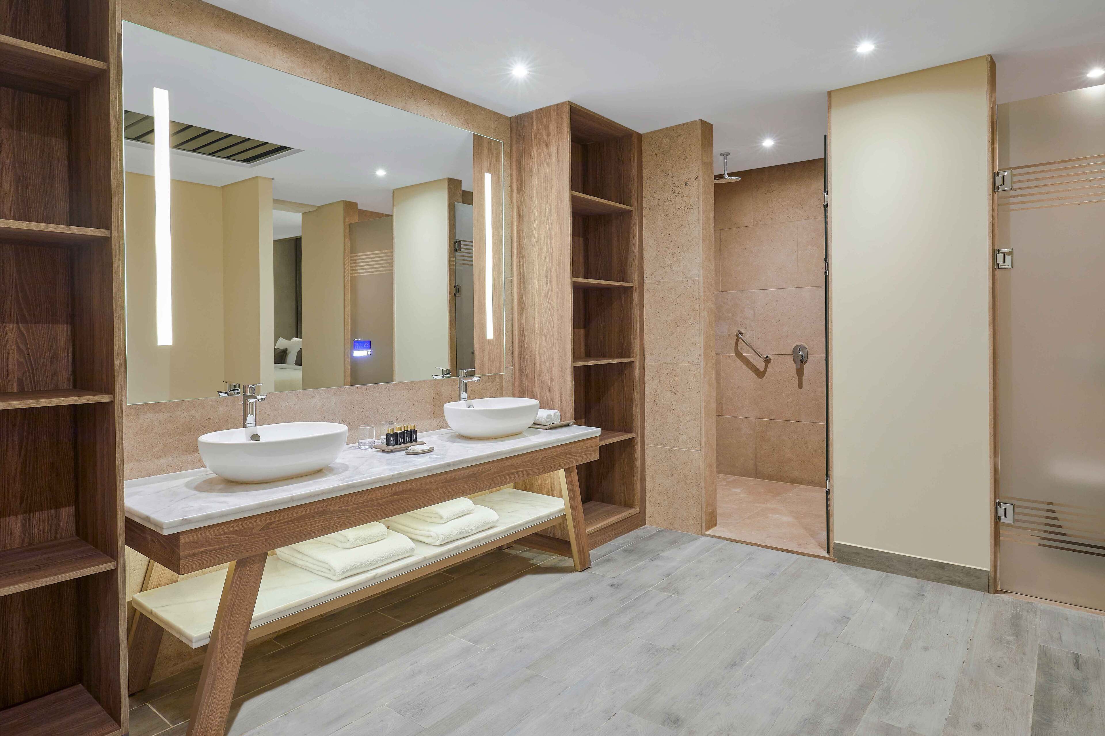 A modern bathroom with two sinks, a large mirror, and a walk-in shower.