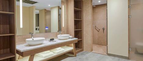 A modern bathroom with two sinks, a large mirror, and a walk-in shower.