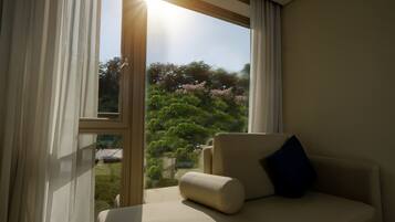 Una habitación con sofá y ventana con vista a un jardín con árboles y flores rosadas.