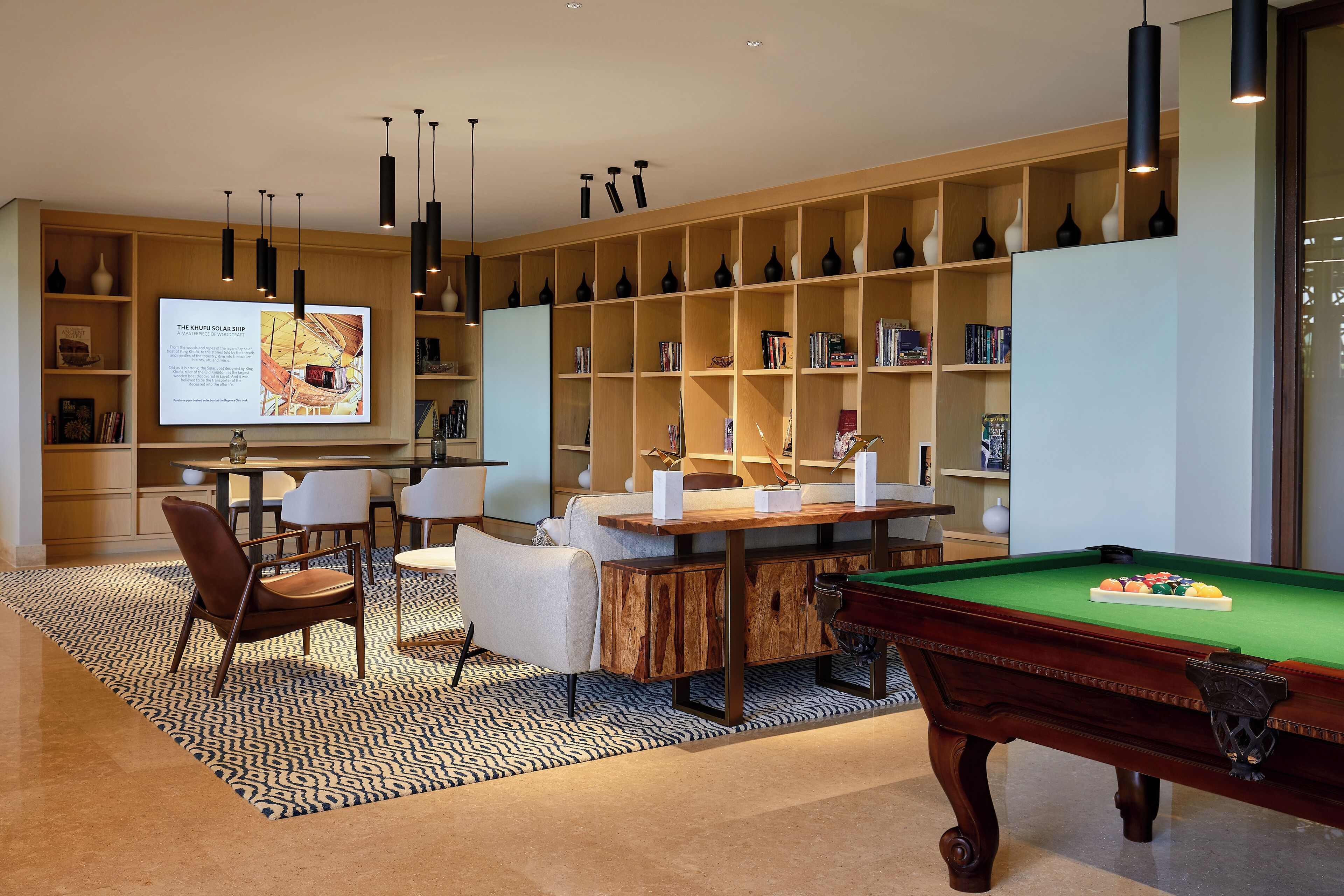 Una sala de estar moderna con mesa de billar, comedor y una estantería llena de libros y objetos decorativos.