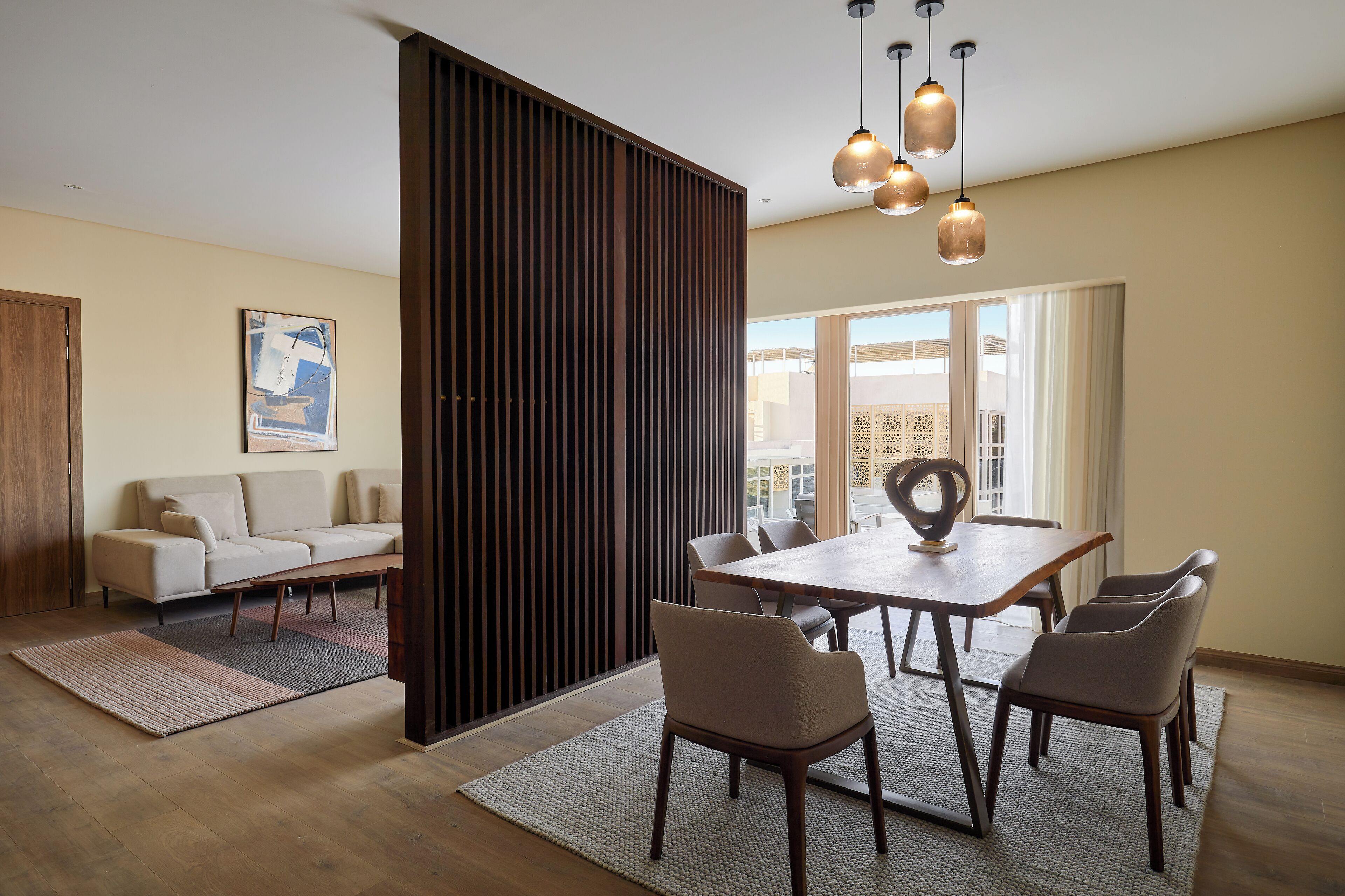 Uma sala de jantar moderna com uma mesa e cadeiras de madeira, um sofá e uma janela grande com vista.