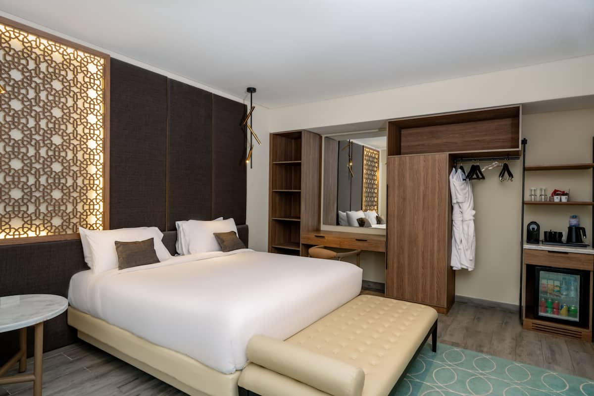 A modern hotel room with a large bed, a desk, a vanity, and a walk-in closet.