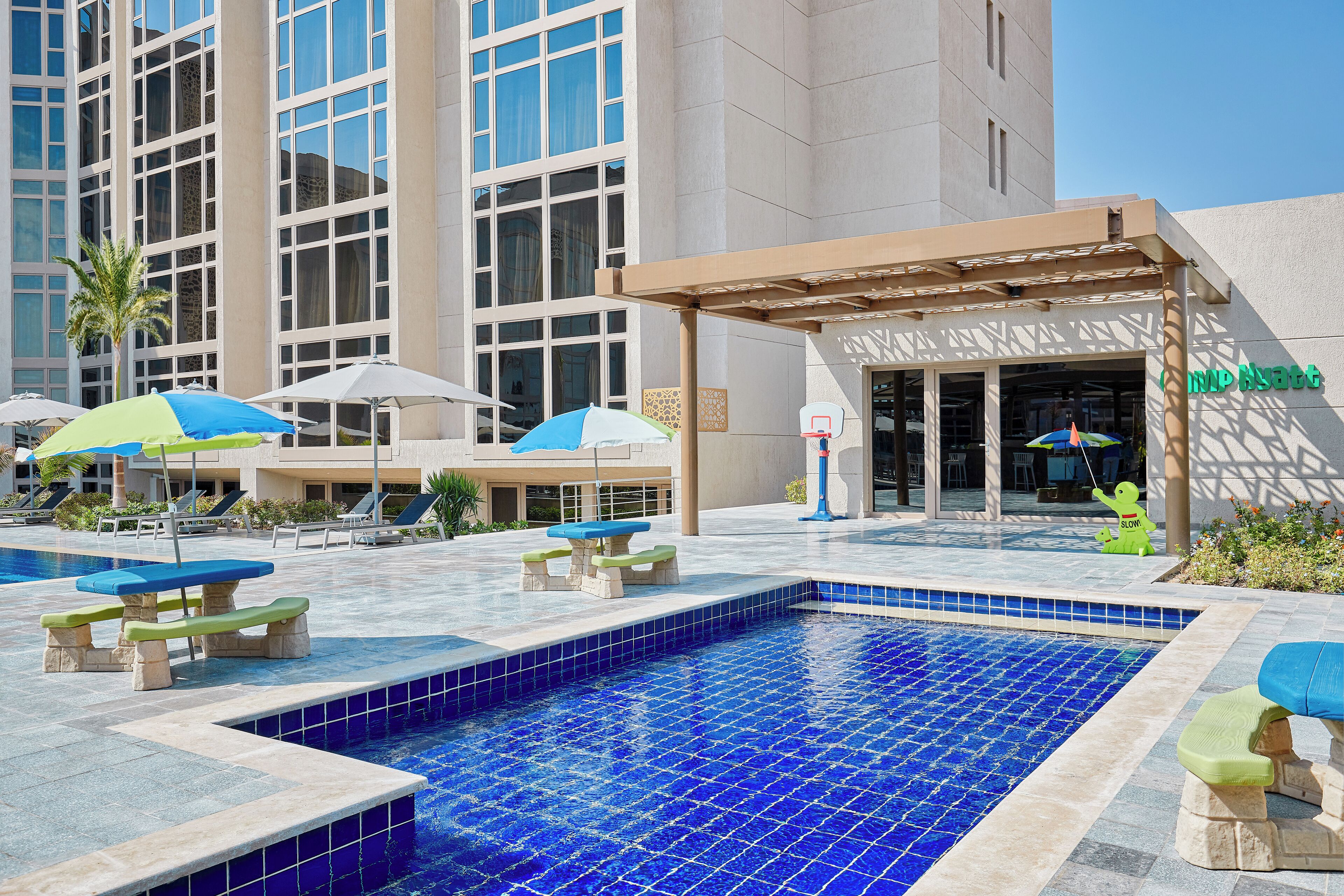 A hotel pool area with a clear view of the building, outdoor seating, and umbrellas.