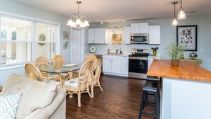 A modern kitchen with white cabinets, a stainless steel oven, and a microwave. There is a dining area with wicker chairs and a glass table.