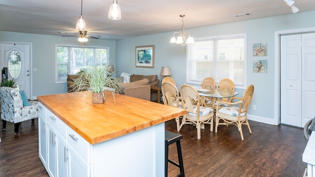 A spacious kitchen with a central island, dining area with wicker chairs, and a ceiling fan.