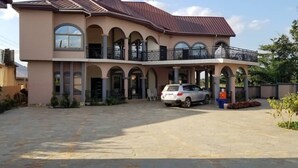 A two-story building with a covered parking area, a car, and a small garden. - Osaah Bema lodge (Antoa)