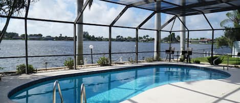 Piscina com vista para um lago, rodeada por uma área coberta com cadeiras e uma mesa.