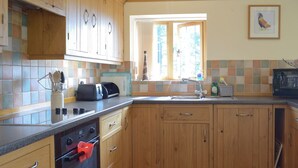 Eine Küche mit Holzausstattung, einer gefliesten Spritzschutzwand, einem Fenster mit Vorhängen und einem Toaster auf der Arbeitsplatte.