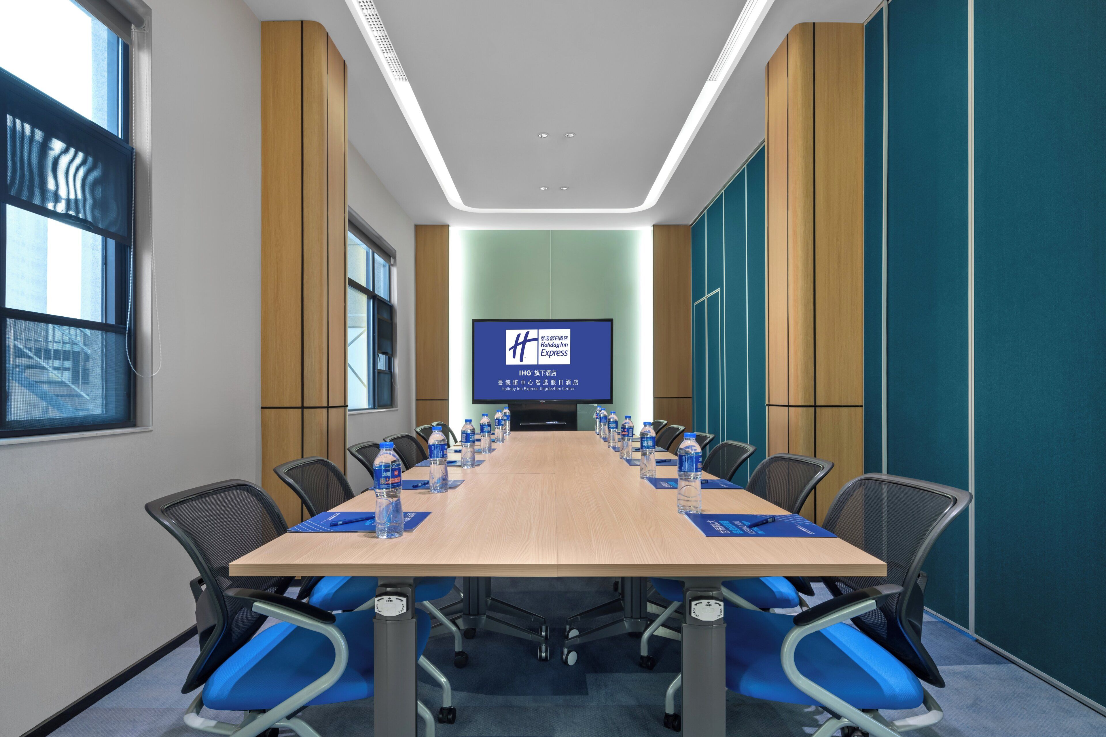 Un salón de conferencias con una larga mesa, sillas, una pantalla y vistas al exterior.