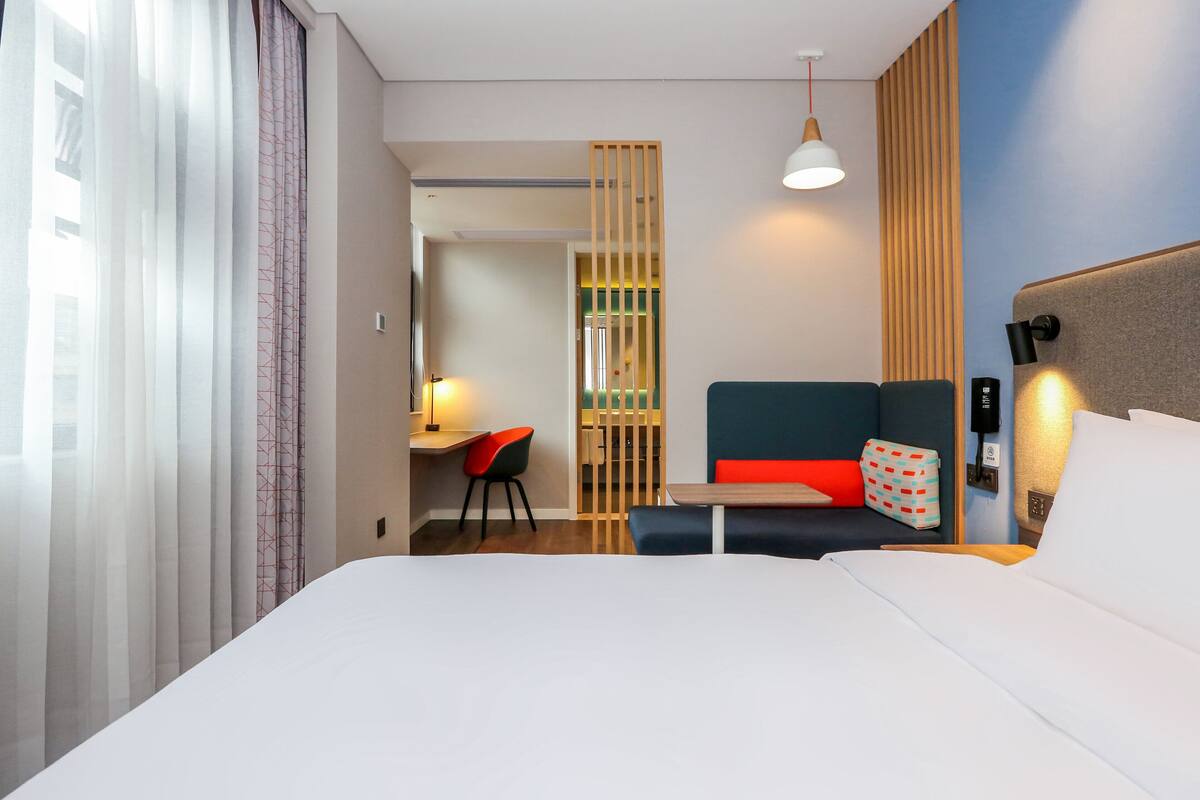 A hotel room with a bed, a desk, a chair, and a seating area with cushions.
