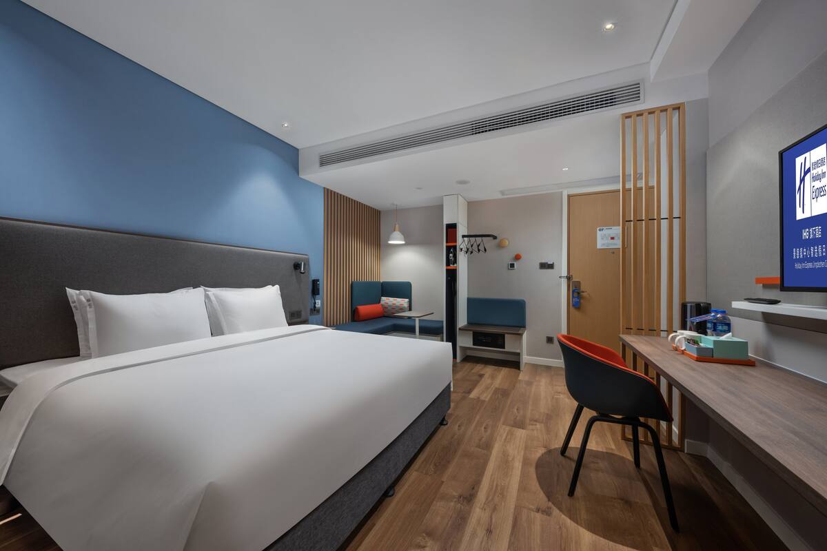 A modern hotel room with a large bed, a desk, and a chair.