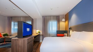 A modern hotel room with a large bed, a desk with a flat-screen TV, and a seating area with a small table and chairs. - Holiday Inn Express Jingdezhen Taoxichuan by IHG (Jingdezhen)