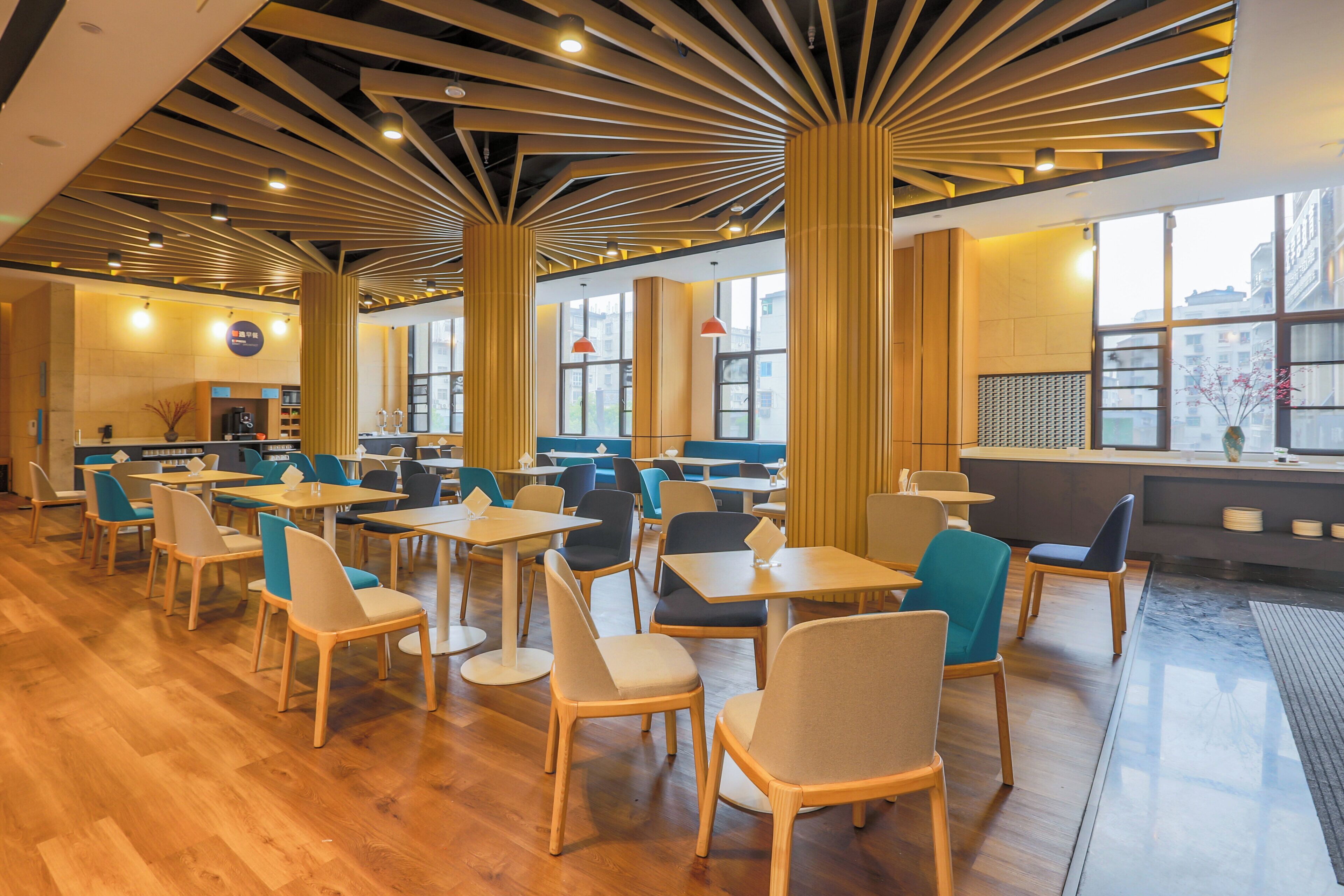 A modern interior with wooden flooring, multiple seating areas, and large windows allowing natural light.