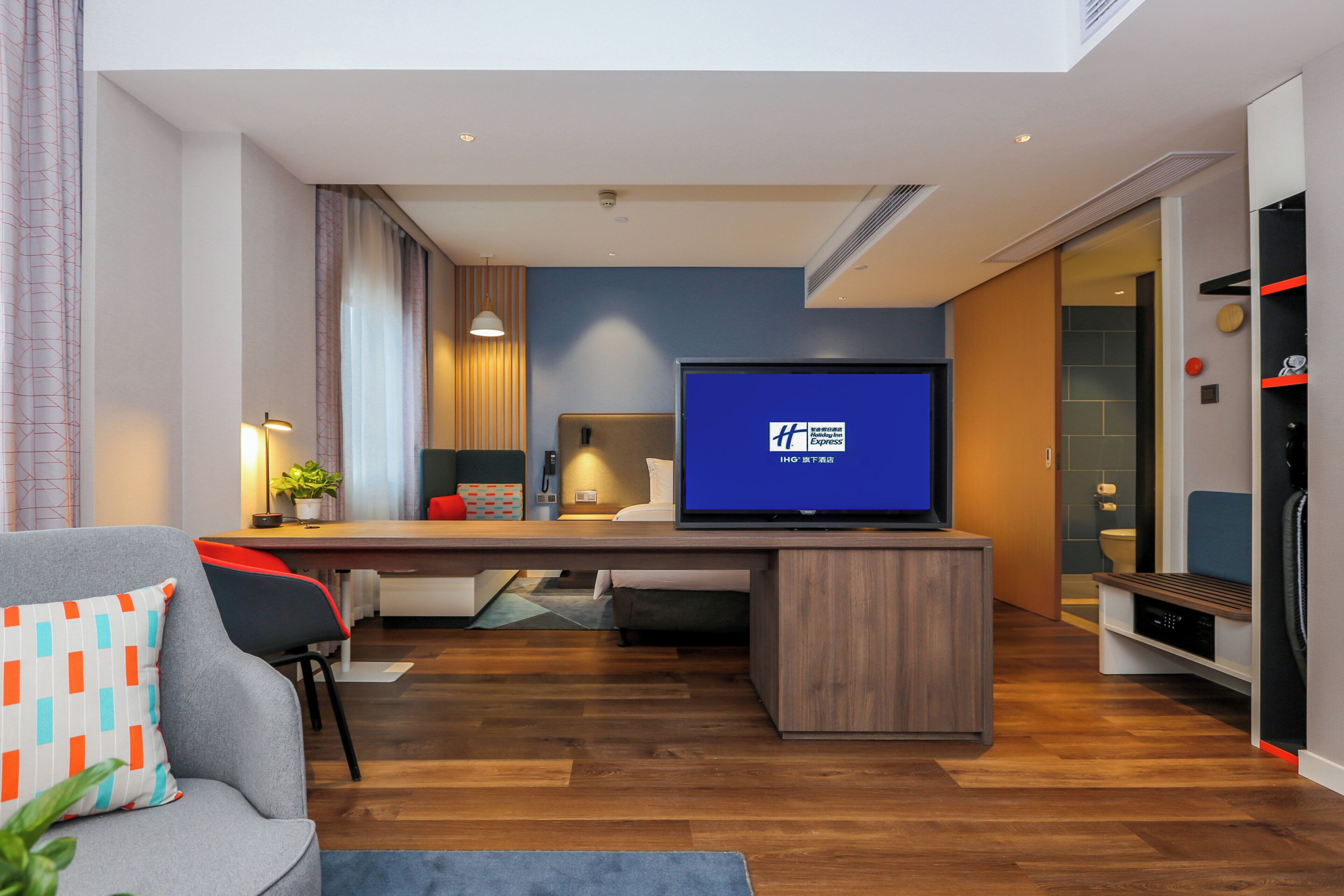 A modern hotel room with a flat-screen TV, a desk, a sofa, and a small table.