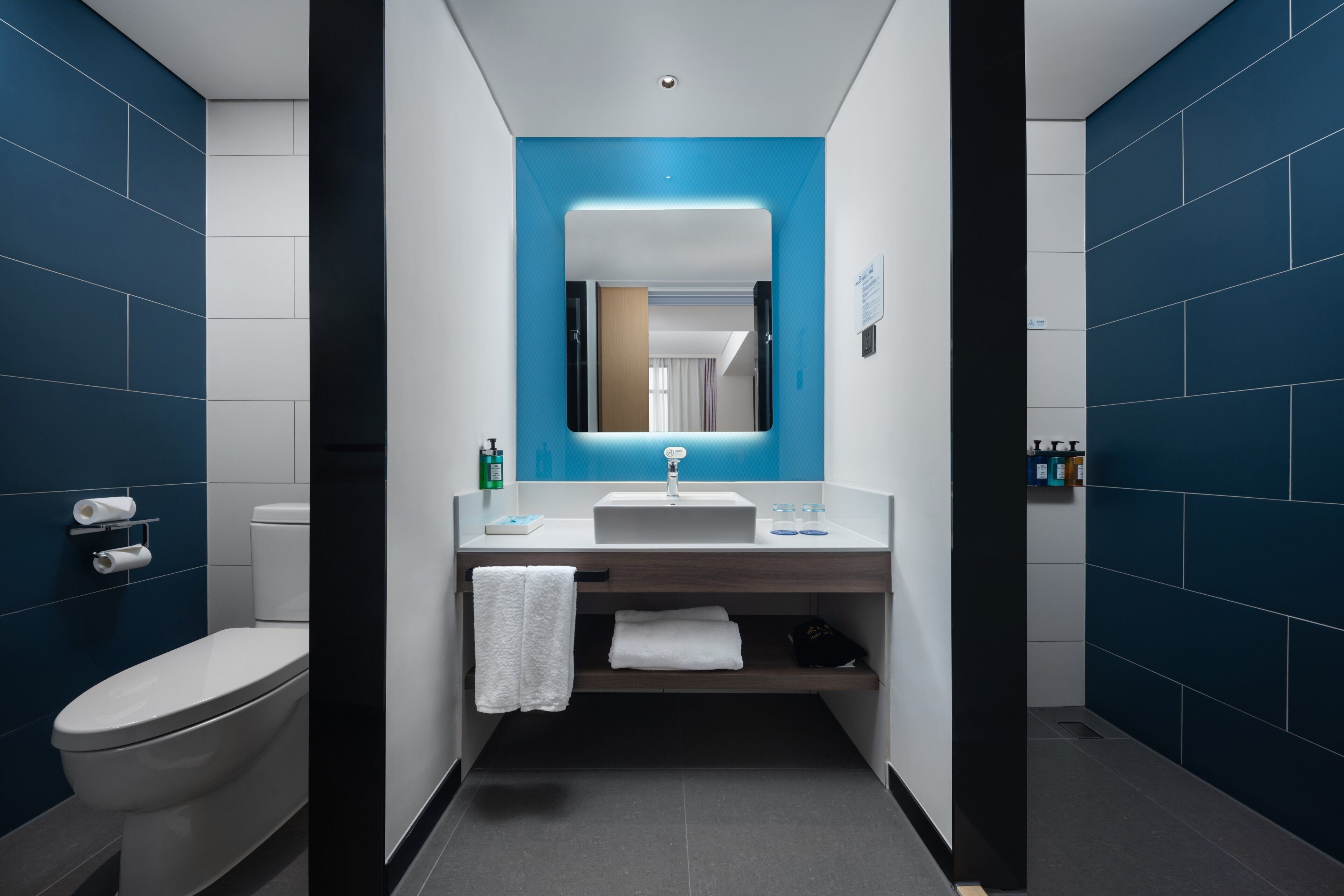 Een moderne badkamer met een wit toilet, een wastafel met spiegel erboven en een blauwe accentmuur.